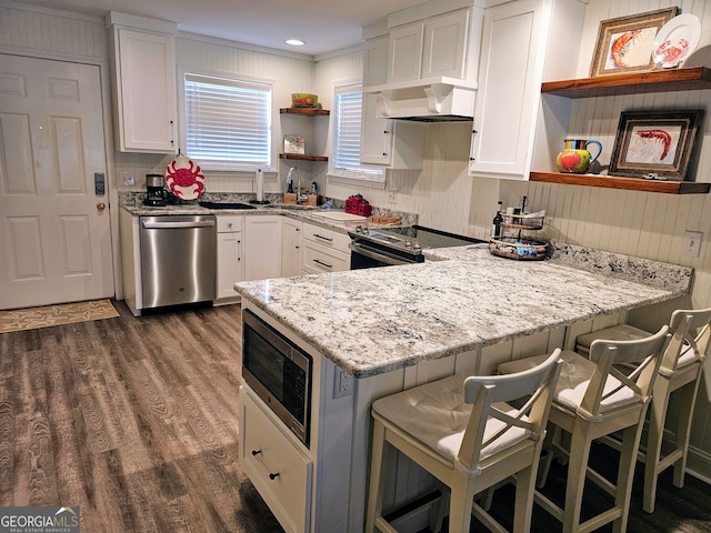 kitchen featuring kitchen peninsula, dark hardwood / wood-style flooring, stainless steel appliances, white cabinetry, and a breakfast bar area