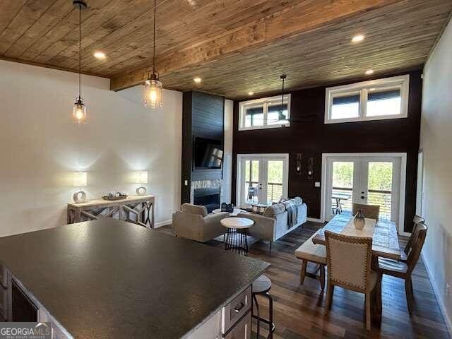 dining space with wooden ceiling, dark wood-type flooring, a high ceiling, french doors, and a large fireplace