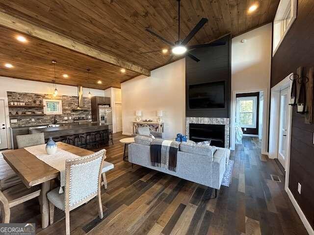 living room with a high ceiling, ceiling fan, dark wood-type flooring, and wood ceiling