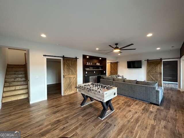 recreation room with a barn door, dark hardwood / wood-style floors, and ceiling fan