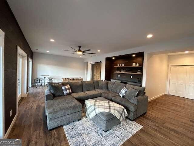 living room with dark hardwood / wood-style flooring, a barn door, and ceiling fan