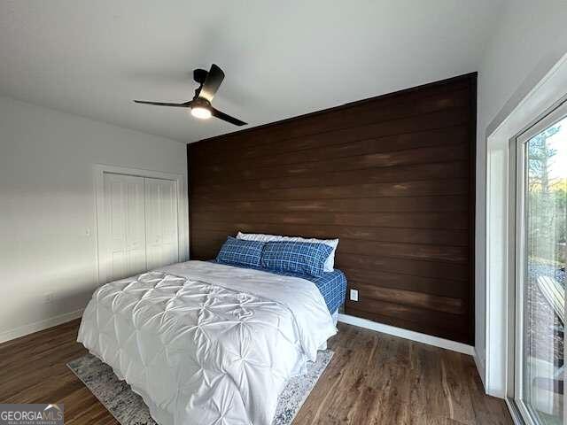 bedroom with ceiling fan, a closet, dark hardwood / wood-style flooring, and wood walls