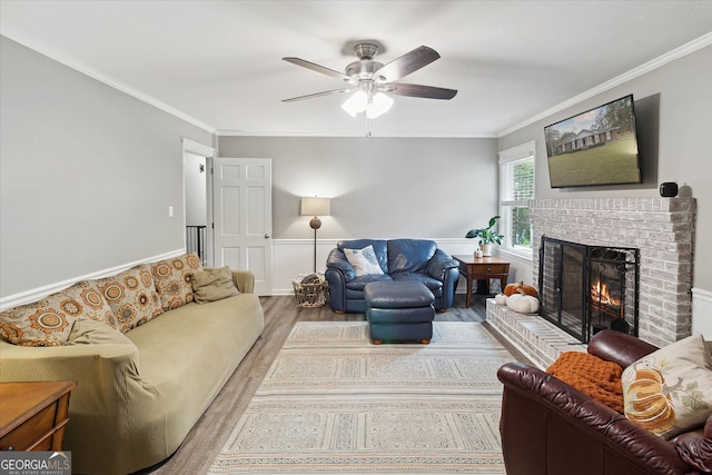 living room featuring a brick fireplace, ceiling fan, crown molding, and light hardwood / wood-style flooring