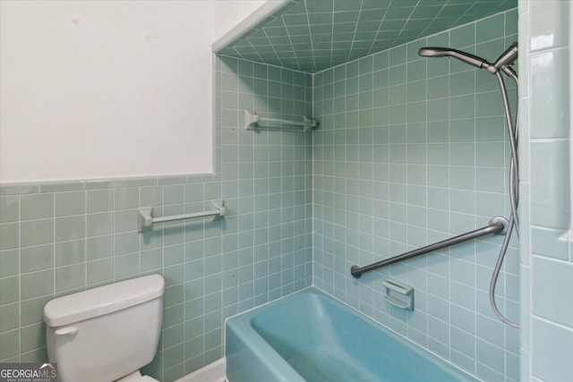 bathroom featuring tiled shower / bath combo, toilet, and tile walls