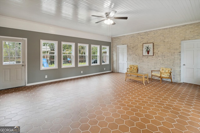 unfurnished room with ceiling fan, plenty of natural light, ornamental molding, and brick wall