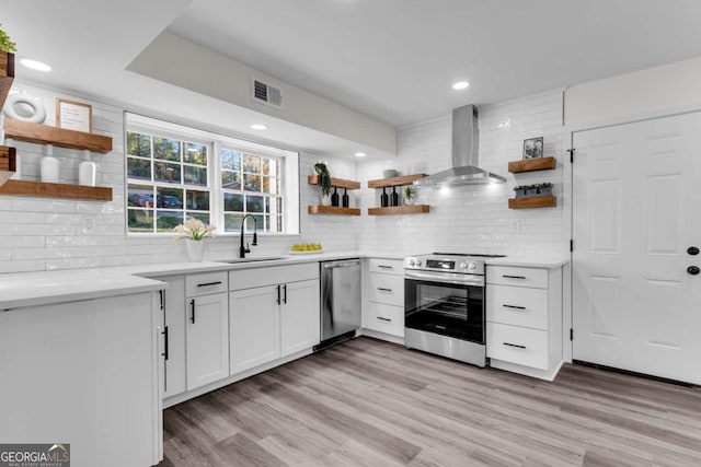 kitchen featuring sink, stainless steel appliances, wall chimney range hood, light hardwood / wood-style floors, and white cabinets