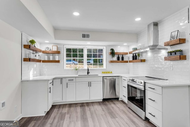 kitchen with white cabinetry, sink, wall chimney exhaust hood, appliances with stainless steel finishes, and light wood-type flooring