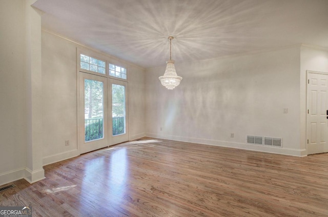 empty room with hardwood / wood-style flooring, a notable chandelier, and ornamental molding