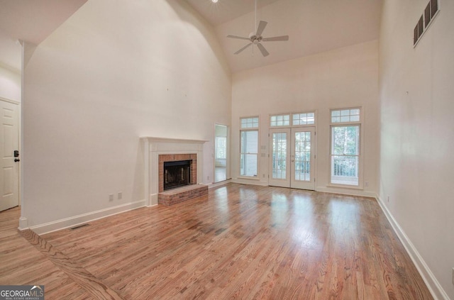 unfurnished living room with ceiling fan, french doors, a brick fireplace, high vaulted ceiling, and light hardwood / wood-style floors