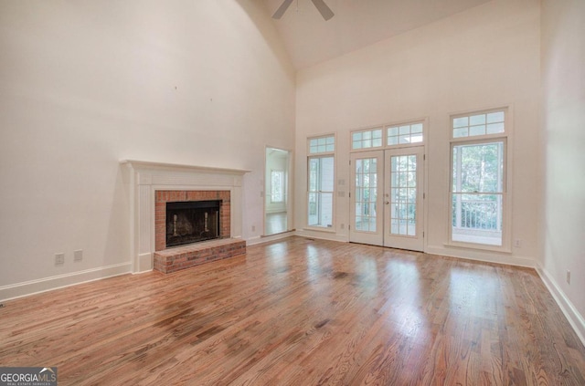 unfurnished living room featuring ceiling fan, french doors, a brick fireplace, high vaulted ceiling, and light hardwood / wood-style floors