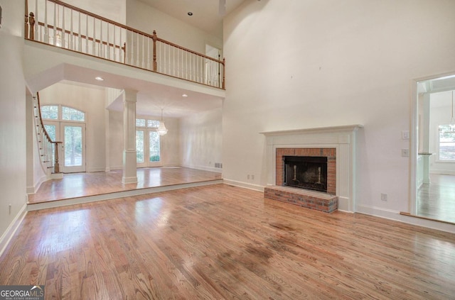 unfurnished living room with hardwood / wood-style flooring, a towering ceiling, and a brick fireplace