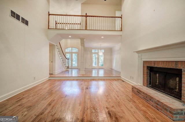 unfurnished living room featuring hardwood / wood-style flooring, a towering ceiling, french doors, and a brick fireplace