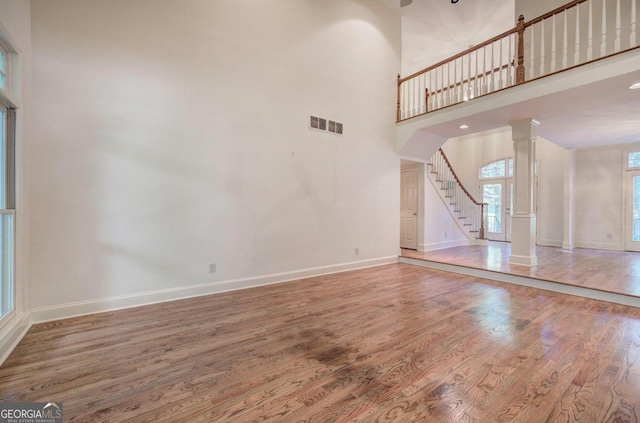 unfurnished living room with a towering ceiling, hardwood / wood-style flooring, and decorative columns