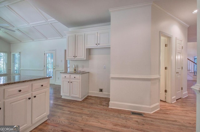 kitchen featuring white cabinetry, crown molding, light stone countertops, and light wood-type flooring