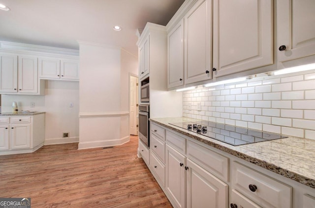 kitchen featuring white cabinetry, stainless steel oven, light stone countertops, black electric stovetop, and ornamental molding