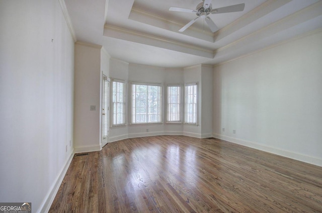 empty room with ceiling fan, wood-type flooring, ornamental molding, and a tray ceiling