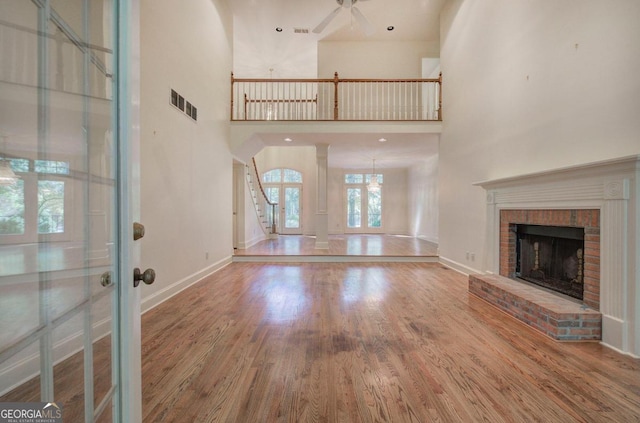 unfurnished living room with ceiling fan, french doors, a brick fireplace, a towering ceiling, and wood-type flooring