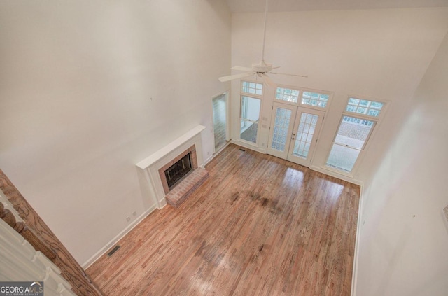 unfurnished living room featuring a towering ceiling, light hardwood / wood-style flooring, and a brick fireplace