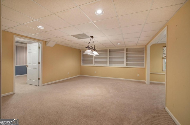 unfurnished room featuring a paneled ceiling, built in features, and light colored carpet