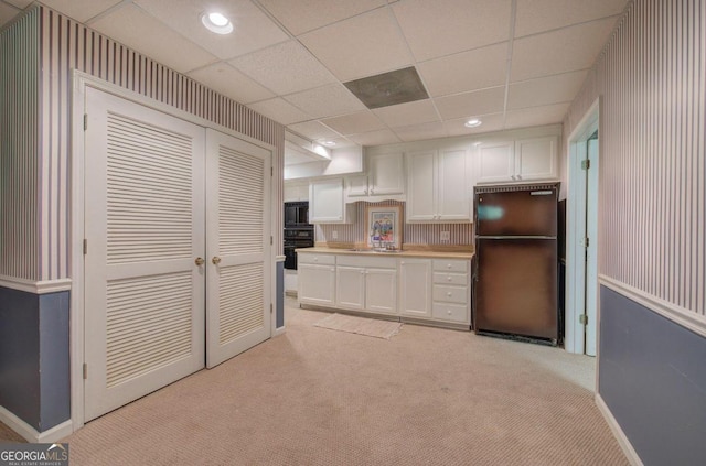 kitchen with light carpet, a drop ceiling, sink, black appliances, and white cabinets