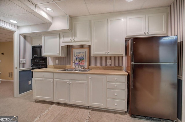 kitchen with a paneled ceiling, light carpet, white cabinets, sink, and stainless steel fridge