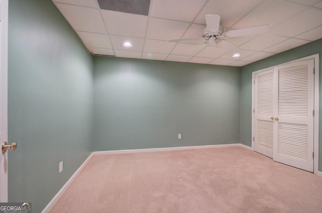 spare room with ceiling fan, a drop ceiling, and light colored carpet