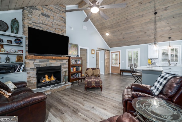 living room with ceiling fan with notable chandelier, a barn door, light hardwood / wood-style floors, and wooden ceiling