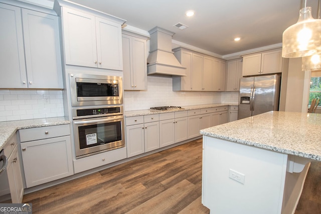 kitchen with light stone counters, dark hardwood / wood-style flooring, decorative light fixtures, appliances with stainless steel finishes, and custom exhaust hood