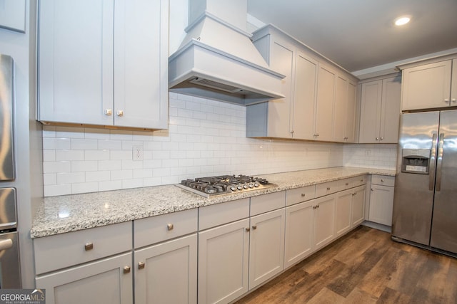 kitchen featuring light stone countertops, dark hardwood / wood-style flooring, backsplash, custom range hood, and stainless steel appliances