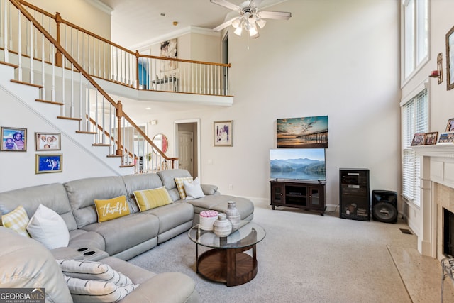 carpeted living room featuring a high end fireplace, a high ceiling, ceiling fan, and ornamental molding