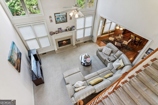 carpeted living room with a fireplace, a high ceiling, ceiling fan, and a healthy amount of sunlight