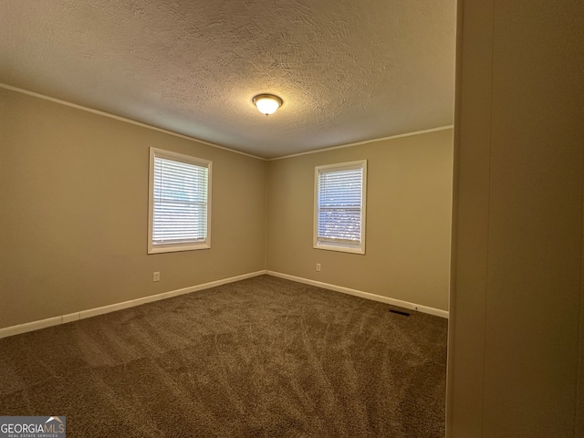 spare room featuring a textured ceiling, dark carpet, plenty of natural light, and crown molding