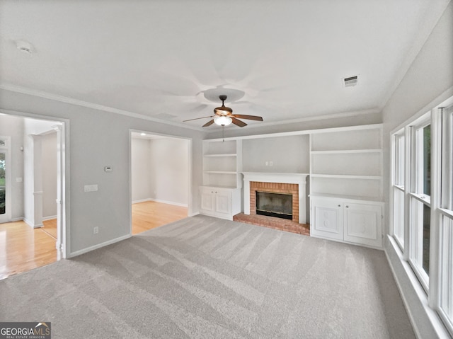 unfurnished living room featuring built in shelves, ceiling fan, crown molding, light carpet, and a fireplace