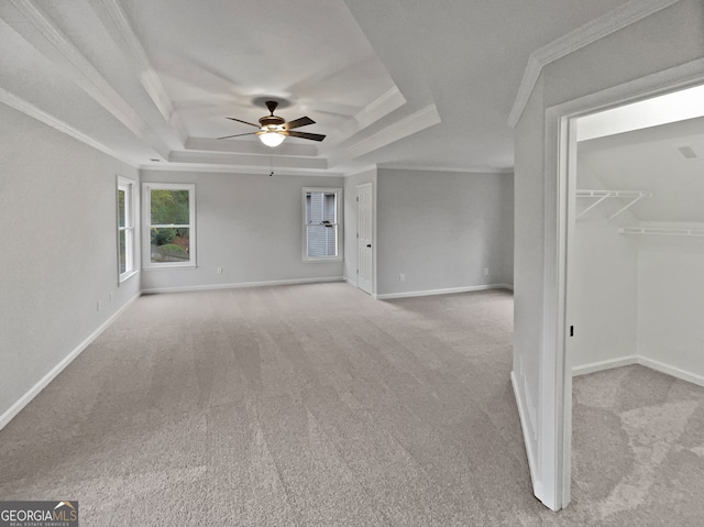 interior space with ceiling fan, a raised ceiling, crown molding, and light carpet