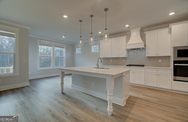 kitchen featuring sink, gas cooktop, decorative light fixtures, a kitchen island with sink, and custom exhaust hood