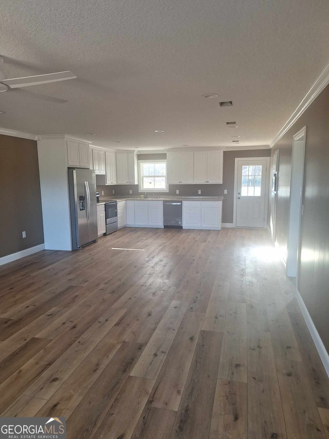 unfurnished living room with hardwood / wood-style flooring, baseboards, a textured ceiling, and ornamental molding