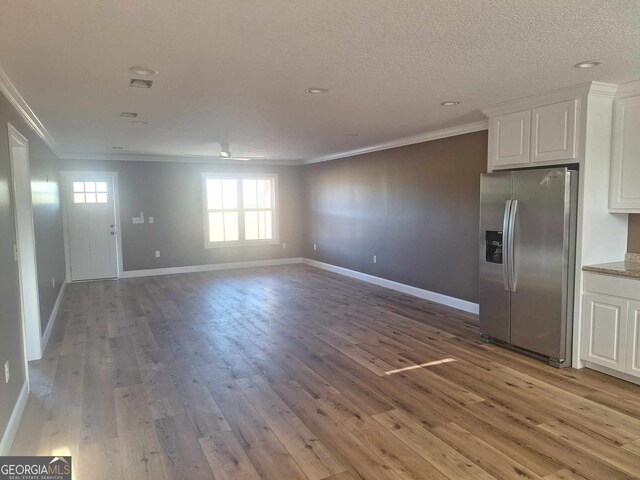 interior space featuring stainless steel refrigerator with ice dispenser, light wood-type flooring, ornamental molding, a textured ceiling, and white cabinetry