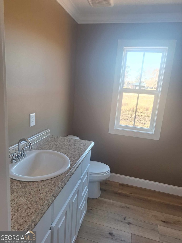 half bath featuring toilet, baseboards, wood finished floors, vanity, and ornamental molding