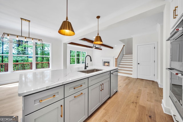 kitchen featuring light hardwood / wood-style floors, stainless steel dishwasher, gray cabinetry, and an island with sink