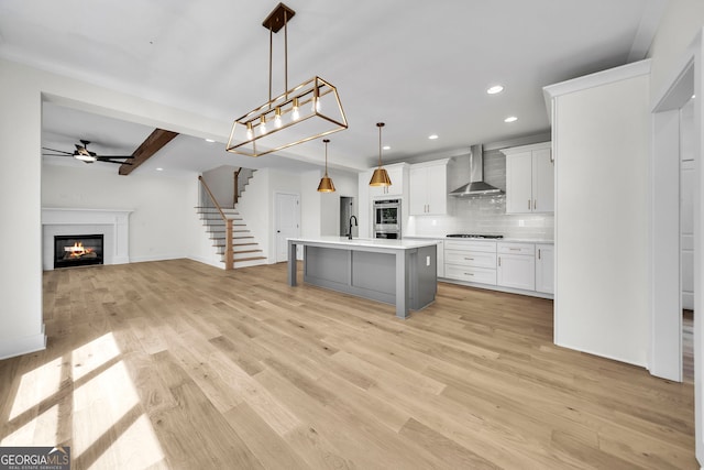 kitchen featuring light wood-style flooring, open floor plan, backsplash, wall chimney range hood, and a sink