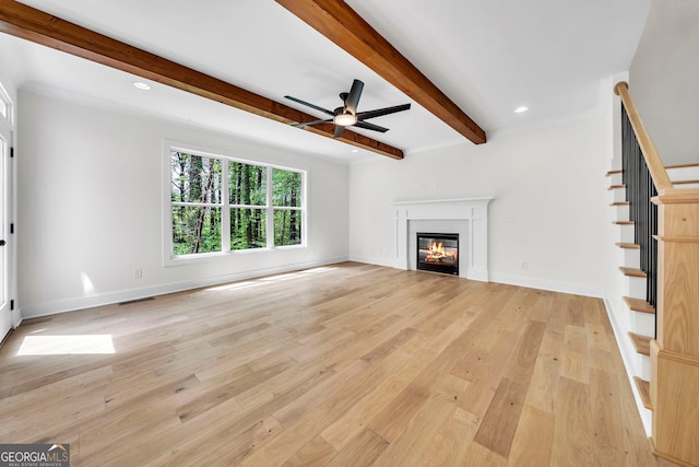 unfurnished living room featuring light wood finished floors, visible vents, a glass covered fireplace, beamed ceiling, and stairs