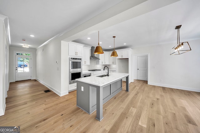 kitchen featuring white cabinets, sink, decorative light fixtures, and an island with sink