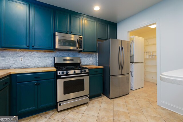 kitchen with butcher block countertops, tasteful backsplash, light tile patterned floors, and stainless steel appliances