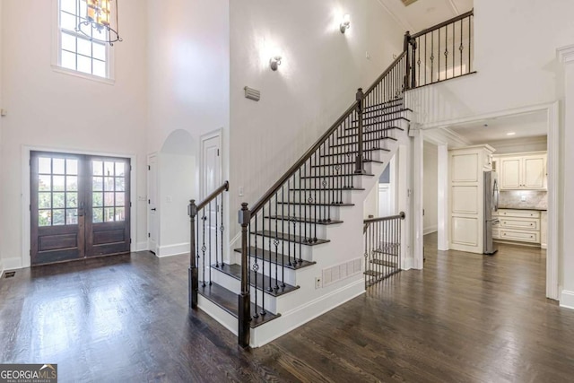 foyer entrance featuring french doors, a towering ceiling, crown molding, a chandelier, and dark hardwood / wood-style floors