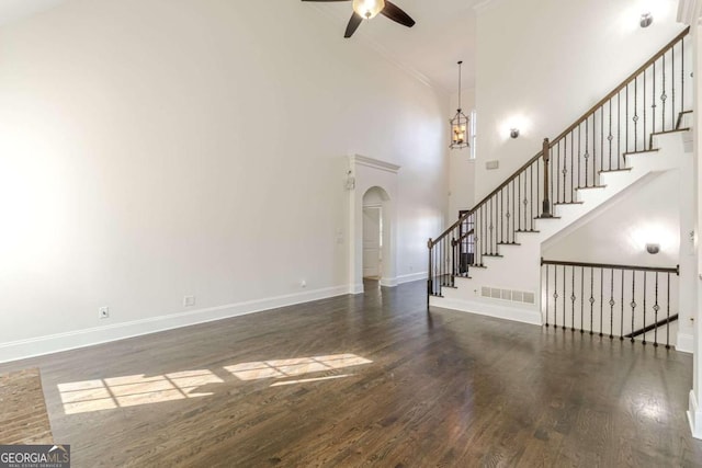 unfurnished living room with ceiling fan, crown molding, dark wood-type flooring, and a high ceiling