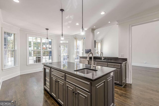 kitchen featuring dark brown cabinetry, sink, hanging light fixtures, dark hardwood / wood-style flooring, and a kitchen island with sink