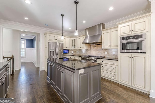 kitchen featuring wall chimney exhaust hood, stainless steel appliances, dark hardwood / wood-style flooring, an island with sink, and pendant lighting