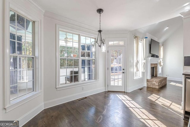 unfurnished dining area featuring crown molding, a fireplace, dark hardwood / wood-style floors, and an inviting chandelier