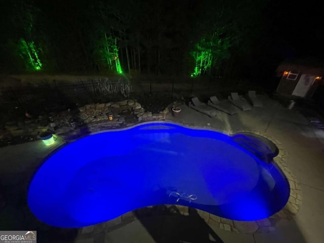 pool at night featuring a patio area