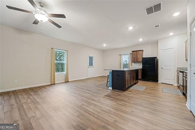 kitchen with a wealth of natural light, black refrigerator, an island with sink, and light wood-type flooring